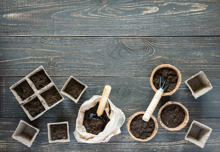 Rakes and eco friendly pots for seedlings on wooden background, small bag with ground and garden trowel and rakesの写真素材