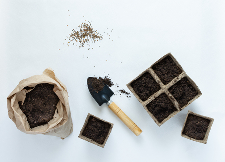 Eco friendly pots for seedlings and seeds on white background, small bag with ground and garden trowelの写真素材