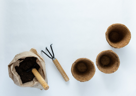 Rakes and eco friendly pots for seedlings on a white background, small bag with ground and garden trowelの写真素材
