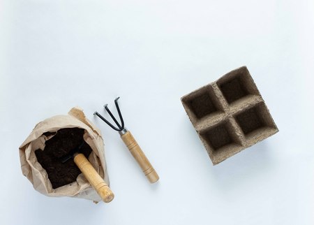 Eco friendly empty pots for seedlings and rakes on white background, small bag with ground and garden trowelの写真素材