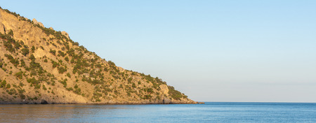 Quiet serene blue sea and wooded mountainsideの写真素材