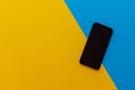 New modern black phone on yellow and blue background, flat lay, copy spaceの写真素材