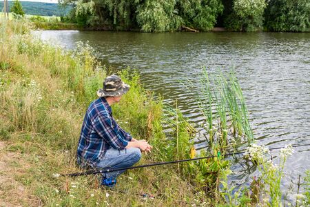 Fisherman fishes on the lake, fisherman man near the water with a fishing rod on a quiet calm eveningの写真素材