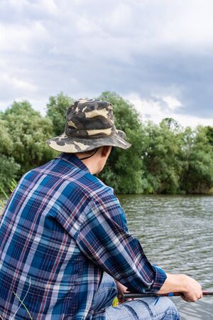 Fisherman fishes on the lake, fisherman man near the water with a fishing rod on a quiet calm eveningの写真素材