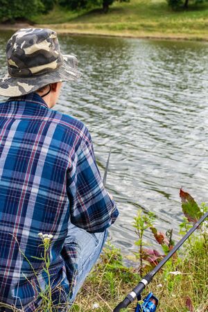 Fisherman fishes on the lake, fisherman man near the water with a fishing rod on a quiet calm eveningの写真素材