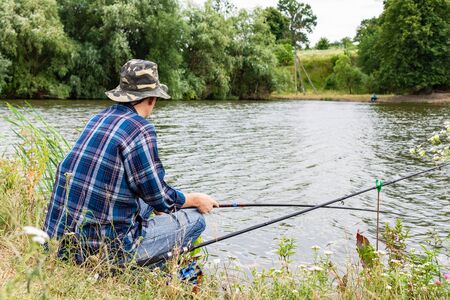 Fisherman fishes on the lake, fisherman man near the water with a fishing rod on a quiet calm eveningの写真素材
