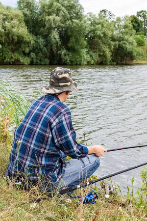Fisherman fishes on the lake, fisherman man near the water with a fishing rod on a quiet calm eveningの写真素材