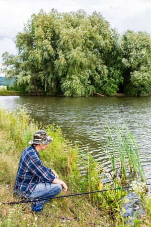 Fisherman fishes on the lake, fisherman man near the water with a fishing rod on a quiet calm eveningの写真素材