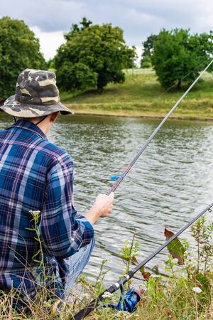 Fisherman fishes on the lake, fisherman man near the water with a fishing rod on a quiet calm eveningの写真素材