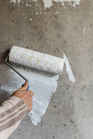 A painter paints a concrete wall with white paint, a male hand with a paint roller for painting a wallの写真素材