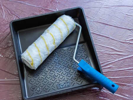 Paint tray and roller on the floor covered with oilclothの写真素材
