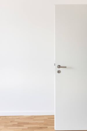 Open white door with a gray chrome handle and keyhole against a white wall in the roomの写真素材