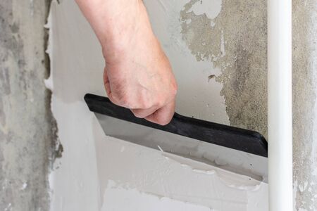 The worker covers the uneven walls, man's hands with a large spatula and putty, apartment repairの写真素材