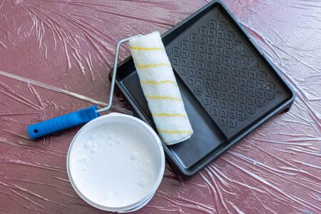 Paint tray with roller and a can of white paint on the floor ,the floor is covered with a oilcloth for protectionの写真素材