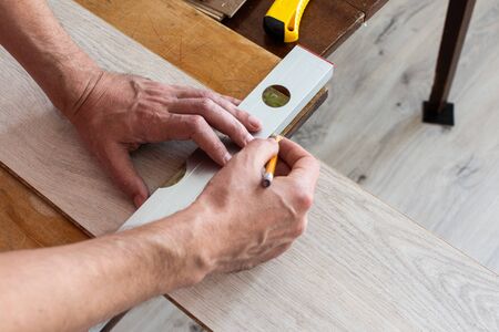 Installation laminate or parquet in the room, worker installing wooden laminate flooring, marking the length of the laminateの写真素材