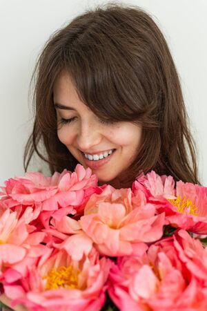 Beautiful girl is happy with flowers on her birthday, face of a girl close up with peonies, valentine's dayの写真素材