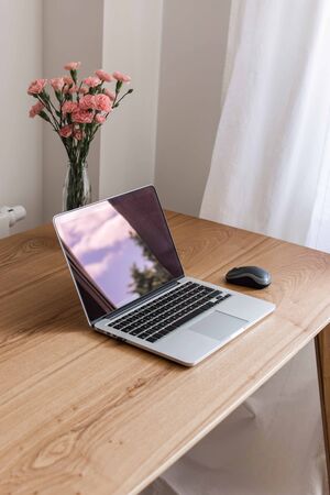 Home interior, home workplace with table and an open laptop close up, flowers in a vaseの写真素材