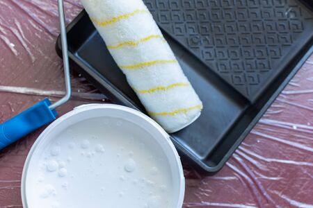 Paint tray with roller and a can of white paint on the floor ,the floor is covered with a oilcloth for protectionの写真素材