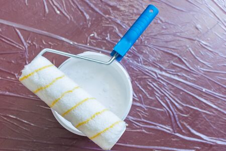 Paint roller and a can of white paint on the floor ,the floor is covered with a oilcloth for protectionの写真素材
