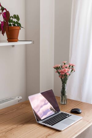 Home interior, home workplace with table and an open laptop close up, flowers in a vaseの写真素材