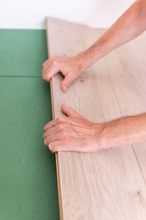 Installation laminate or parquet in the room, worker installing wooden laminate flooring, environmentally friendly soundproofing sheetsの写真素材