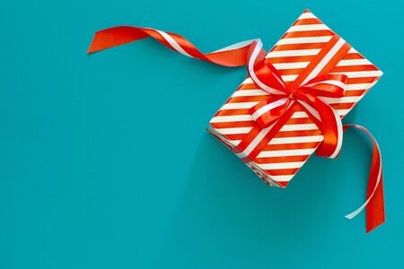Festive background with red and white striped gift, gift box with ribbon and bow on a blue turquoise background, flat lay, top viewの写真素材