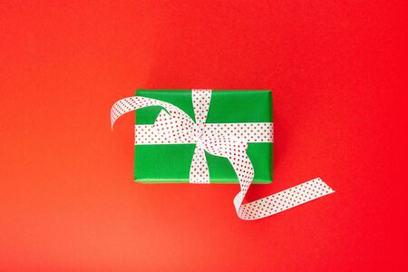 Festive background with gift, green gift box with ribbon in polka dots and bow on red background, flat lay, top viewの写真素材