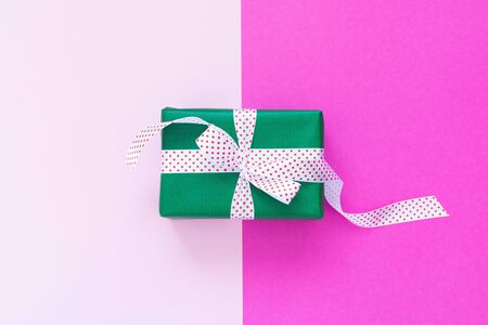 Festive background with gift, green gift box with ribbon in polka dots and bow on pink background, flat lay, top viewの写真素材