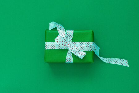 Festive background with gift, gift box with ribbon in polka dots and bow on green background, flat lay, top viewの写真素材
