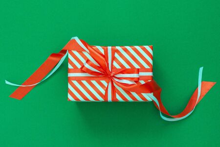 Festive background with red and white striped gift, gift box with ribbon and bow on green background, flat lay, top viewの写真素材
