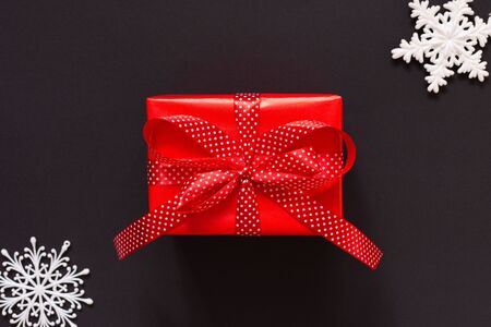 Festive background with gift, red gift box with ribbon in polka dots and bow and snowflakes on black background, black friday concept, flat lay, top viewの写真素材