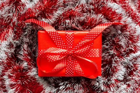 Holiday background with red bright shiny Christmas garland and gift box with ribbon in polka dots and bowの写真素材