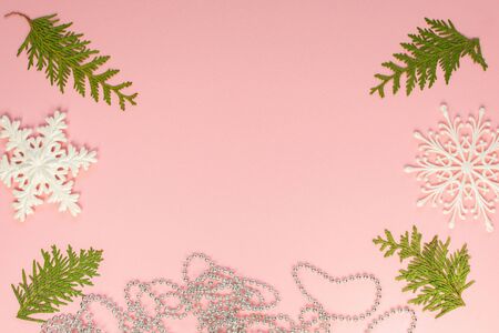 Festive christmas background, fir branches and white snowflakes and silver decorative beads on pink background, flat lay, top viewの写真素材