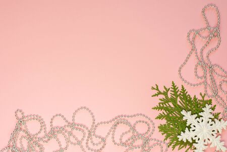 Festive christmas background, fir branches and white snowflakes and silver decorative beads on pink background, flat lay, top viewの写真素材