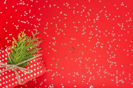 Festive background , red gift box in polka dots with ribbon and bow and thuja twigs on a red background with glitter silver stars, flat lay, top viewの写真素材