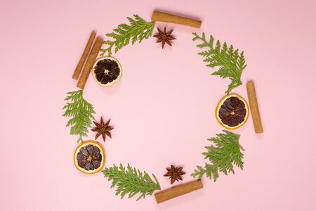 Wreath of fir twigs, star anise and cinnamon sticks and dry citrus on a pink background, christmas holiday background, flat layの写真素材