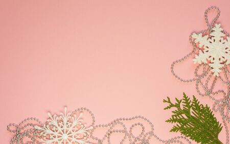 Festive christmas background, fir branches and white snowflakes and silver decorative beads on pink background, flat lay, top viewの写真素材