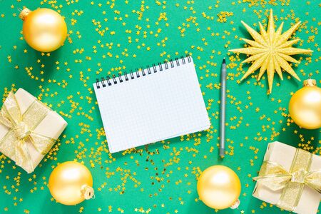Holiday background , gold christmas balls and fir twigs and bright shiny christmas garland on a green background with glitter gold stars, open spiral notepad and pen, flat lay, top viewの写真素材