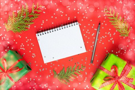Holiday background , gift boxes with ribbon and bow on a red background with glitter silver stars, open spiral notepad and pen, flat lay, top viewの写真素材