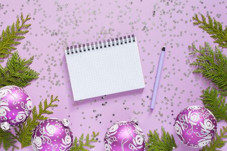 Holiday background , christmas balls and thuja twigs on a lilac background with glitter silver stars, open spiral notepad and pen, flat lay, top viewの写真素材