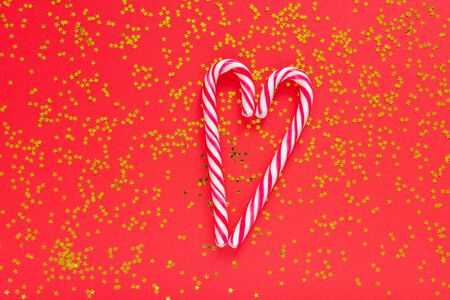 Holiday background, christmas candy cane in the form of a heart on a red background with glitter gold starsの写真素材