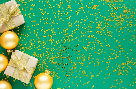 Holiday background , gold christmas balls and gift boxes on a green background with glitter gold stars, flat lay, top viewの写真素材