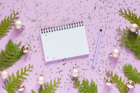 Holiday background , christmas balls and thuja twigs on a lilac background with glitter silver stars, open spiral notepad and pen, flat lay, top viewの写真素材