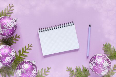 Holiday background , christmas balls and thuja twigs on a lilac background with glitter silver stars, open spiral notepad and pen, flat lay, top viewの写真素材