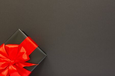 Festive background with gift, black gift box with red ribbon and bow on black background, black friday concept, flat lay, top viewの写真素材