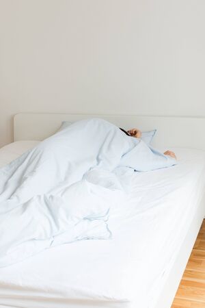 Part of the home or hotel interior, man sleeping on a white bed with blue linens in the morningの写真素材