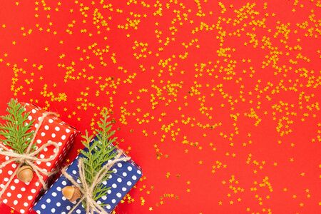 Holiday background , red and blue gift boxes in polka dots with ribbon and bow and thuja twigs on a red background with glitter gold stars, flat lay, top viewの写真素材