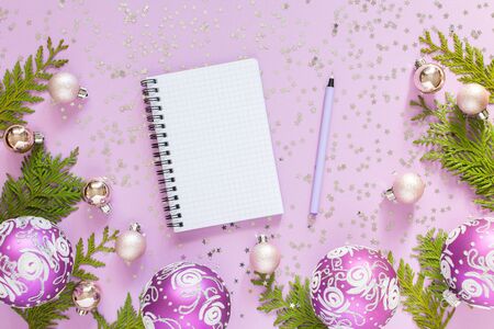 Holiday background , christmas balls and thuja twigs on a lilac background with glitter silver stars, open spiral notepad and pen, flat lay, top viewの写真素材