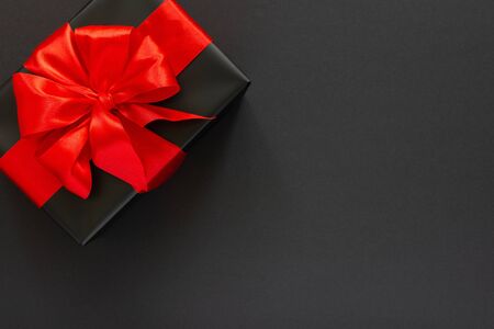Festive background with gift, black gift box with red ribbon and bow on black background, black friday concept, flat lay, top viewの写真素材