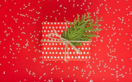 Festive background , red gift box in polka dots with ribbon and bow and thuja twigs on a red background with glitter silver stars, flat lay, top viewの写真素材